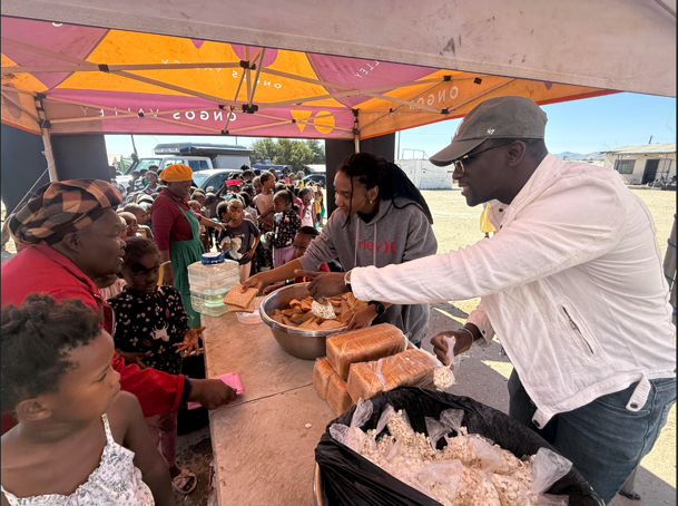 Volunteers serving food to children and families beneath a community tent