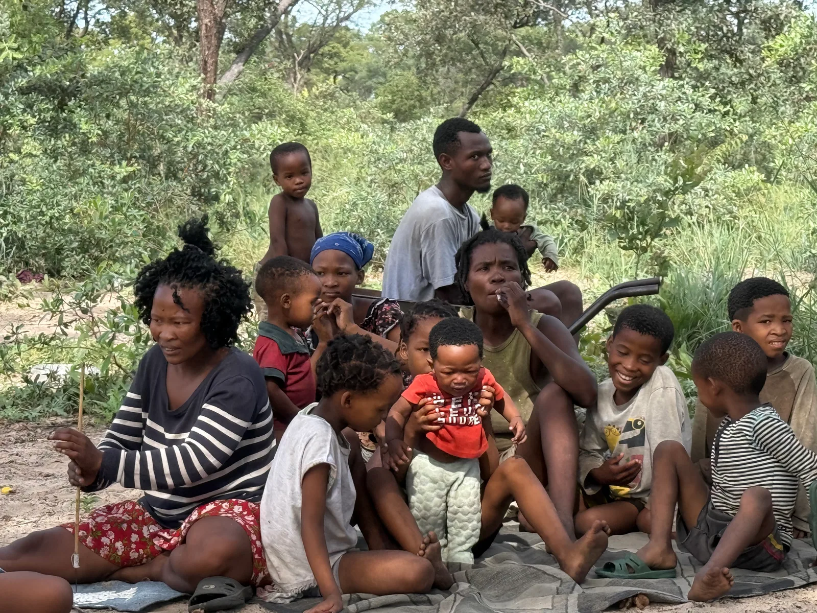 Adults and children gathered together in the shade of trees
